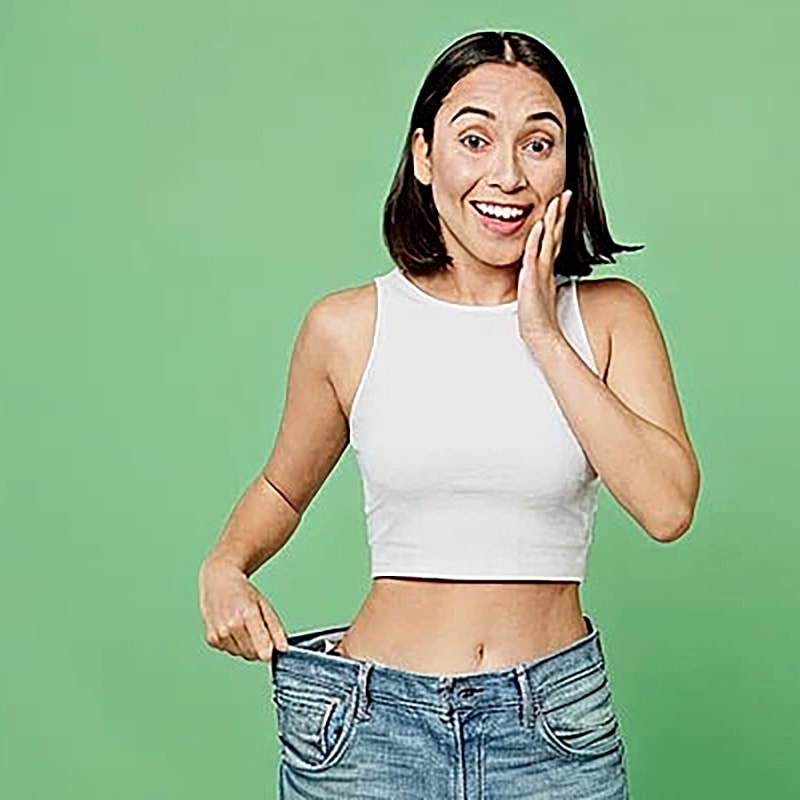 Woman happily showing oversized jeans on green background.