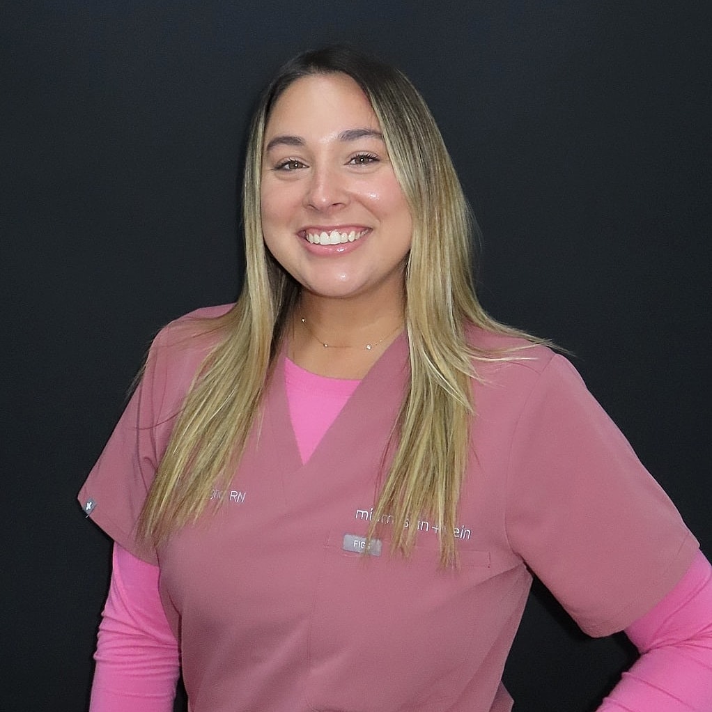 Smiling nurse in scrubs against black background.