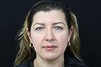 Woman with long hair and neutral expression.