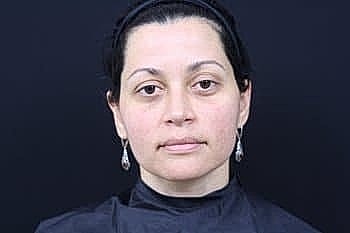Woman with dark hair and earrings against backdrop