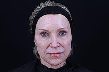 Woman with bare face and headband against black background.