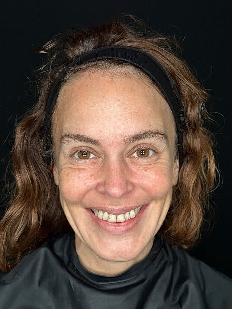 Smiling woman with curly hair against black background.