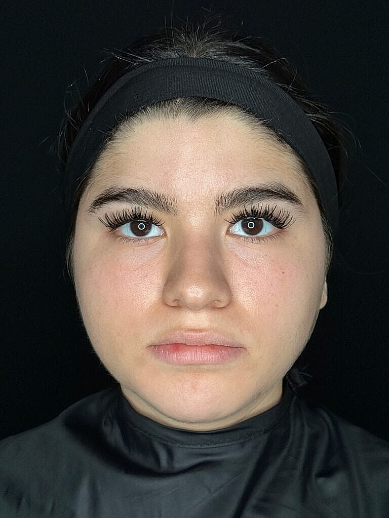 Woman with dramatic eyelashes, neutral expression, dark background.