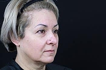 Woman with short hair, neutral expression, black background.