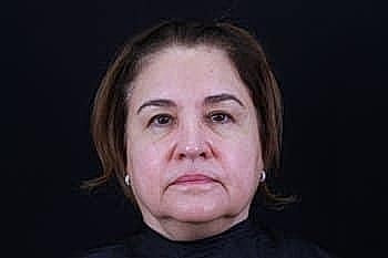 Middle-aged woman with neutral expression against black background.