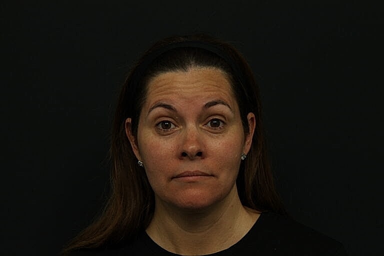 Woman with brown hair, neutral expression, black background.