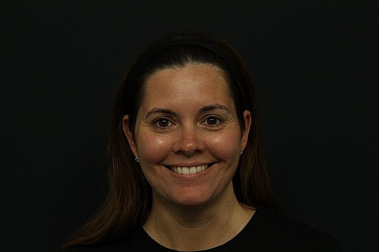 Smiling woman with long brown hair, black background.