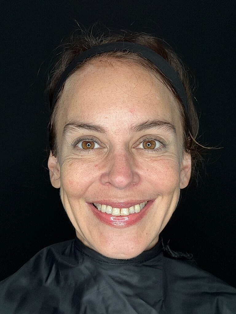 Smiling woman with brown eyes and black background.