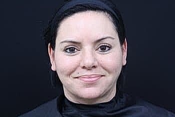 Smiling woman with dark hair on black background.