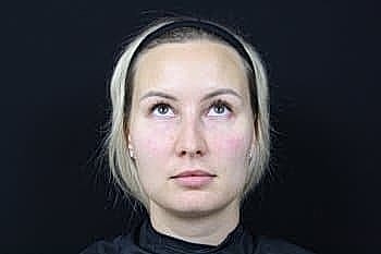 Woman with blonde hair looking upward against black background.