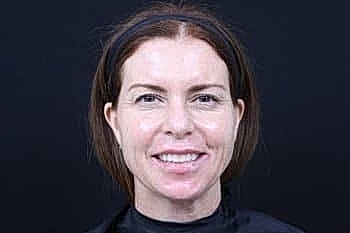 Smiling woman with short brown hair, black background.