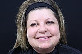 Smiling woman in salon setting with black background.