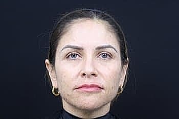 Woman with dark hair and earrings against black background.