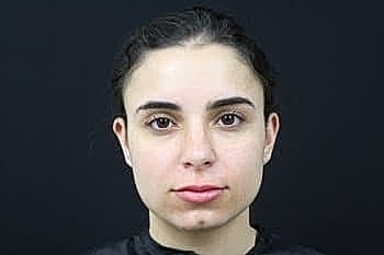 Woman with neutral expression against black background.