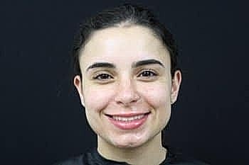 Smiling woman with dark hair on black background.
