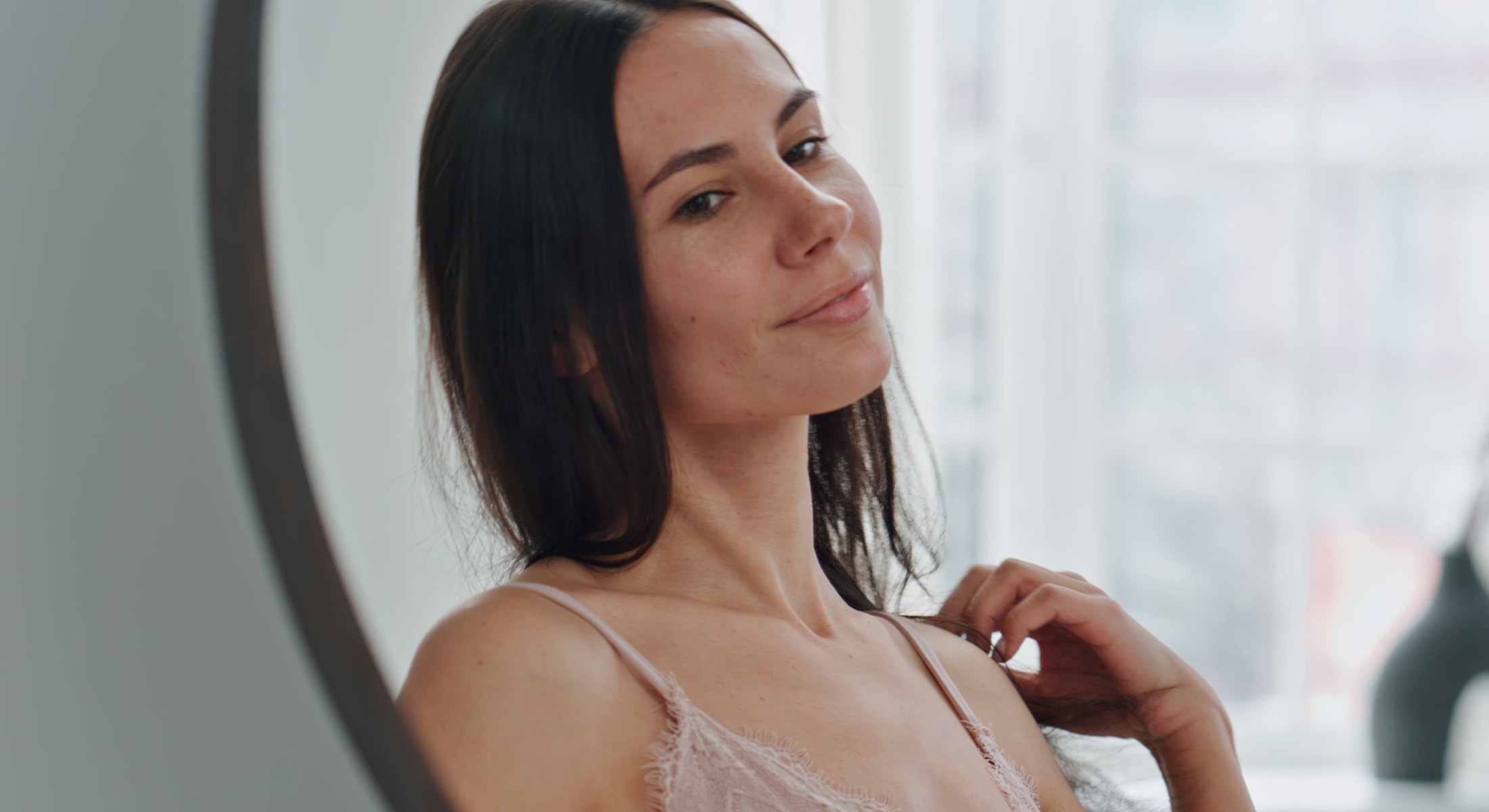 Woman looking into mirror, smiling softly.