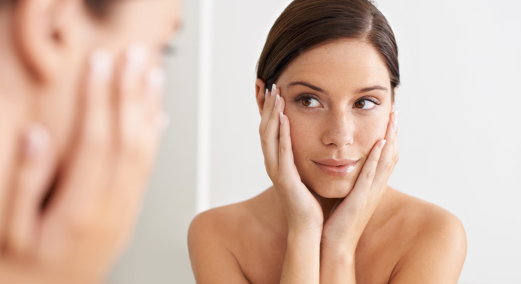 Woman reflecting in a mirror, touching her face.