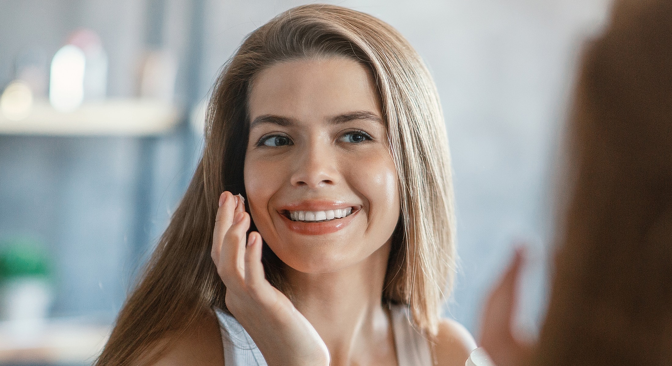 Woman smiling while applying skincare product.